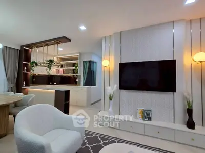 Modern living room with stylish decor and open layout, featuring a large TV and elegant lighting.