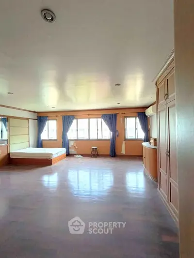 Spacious bedroom with large windows and elegant blue curtains, featuring built-in storage and a cozy atmosphere.