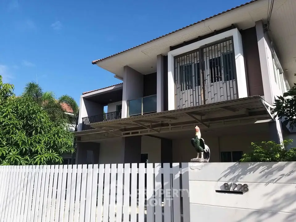 Modern two-story house with balcony and lush greenery