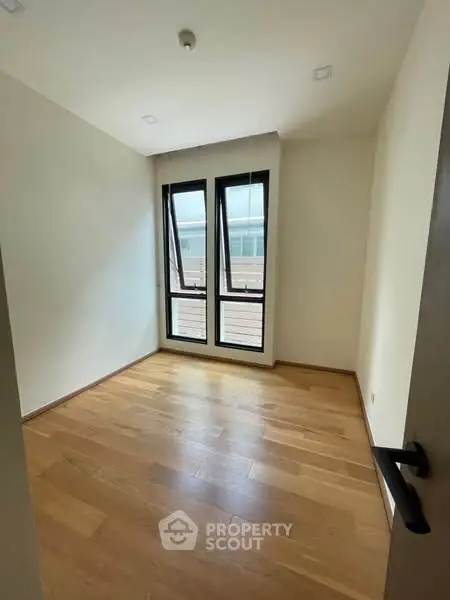 Bright empty room with wooden flooring and large windows in modern apartment.