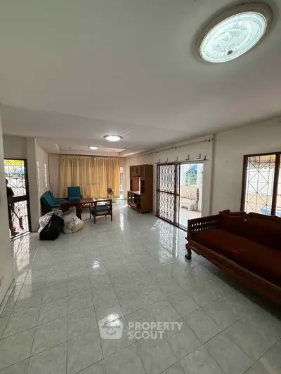 Spacious living room with tiled floors and natural light, featuring classic wooden furniture and large windows.