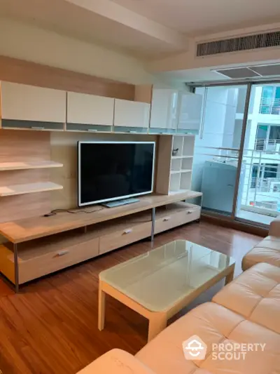 Modern living room with sleek furniture and large TV, featuring floor-to-ceiling windows for natural light.