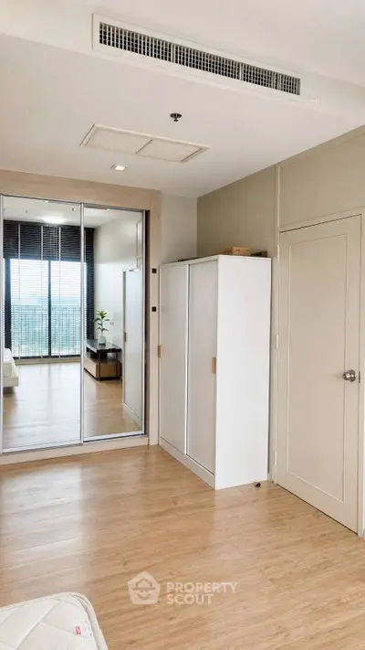 Spacious bedroom with mirrored closet and wooden flooring, offering a glimpse of a balcony with a view.