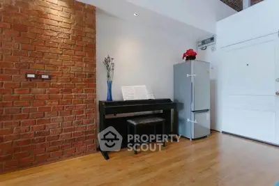 Charming interior with exposed brick wall, piano, and modern fridge in cozy living space.