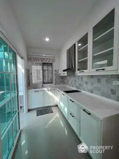 Modern kitchen with sleek white cabinets and glass doors, featuring a closed layout and ample natural light.