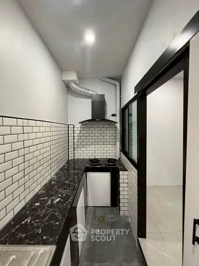 Modern compact kitchen with sleek black countertops and white subway tile backsplash.
