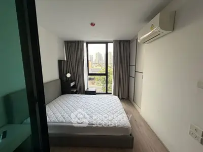 Modern bedroom with city view, featuring a large window, air conditioning, and minimalist decor.