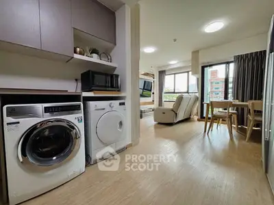 Modern open-plan living room with kitchen featuring washing machine and microwave, bright and spacious interior.