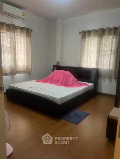 Cozy bedroom with wooden flooring and stylish curtains, featuring a modern bed frame and natural light.