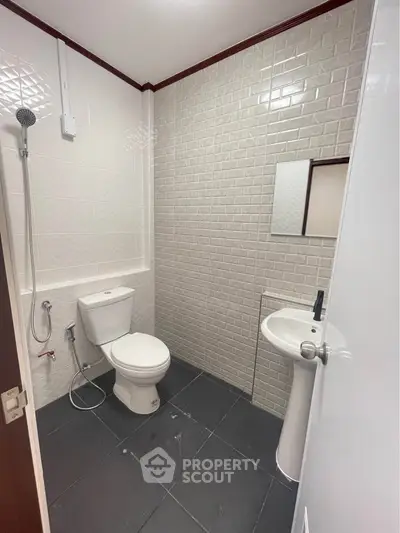 Modern bathroom with sleek white fixtures and textured wall tiles, featuring a shower and pedestal sink.