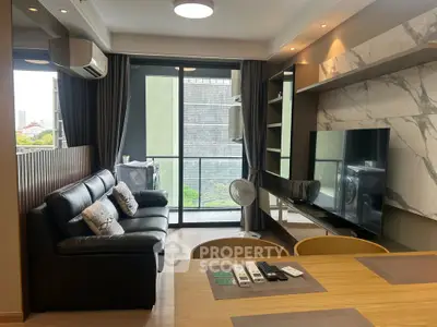 Modern living room with sleek black leather sofa and large TV, featuring a balcony view.