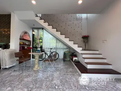 Spacious living area with elegant marble flooring and a modern staircase leading to the upper level, complemented by natural light from the large windows.