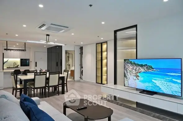 Modern open-plan living room with sleek kitchen and large TV, perfect for entertaining.