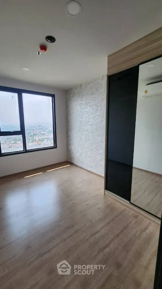 Spacious bedroom with large window and built-in wardrobe offering city views.