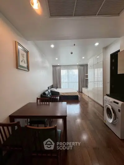 Modern studio apartment with wooden flooring, cozy bed, dining area, and washing machine.