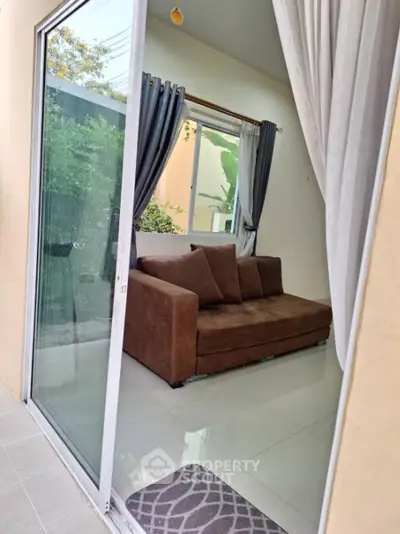 Cozy small living room with brown sofa and glass sliding door opening to garden view.