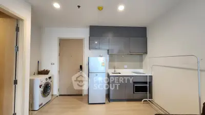 Modern kitchen with sleek cabinets, washing machine, and compact fridge in a cozy apartment.