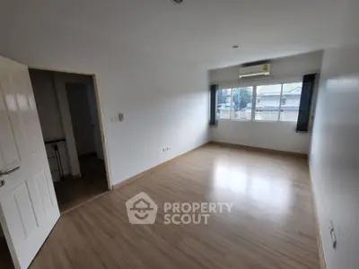 Spacious empty room with wooden flooring and large window, ideal for customization.