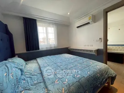 Cozy bedroom with blue floral bedding and air conditioning, featuring natural light from a window.