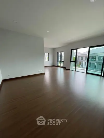 Spacious empty room with large windows and wooden flooring in modern home