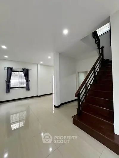Spacious modern interior with elegant staircase and large windows in a well-lit home.