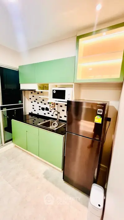 Modern kitchen with sleek green cabinets and stainless steel appliances in a stylish apartment.