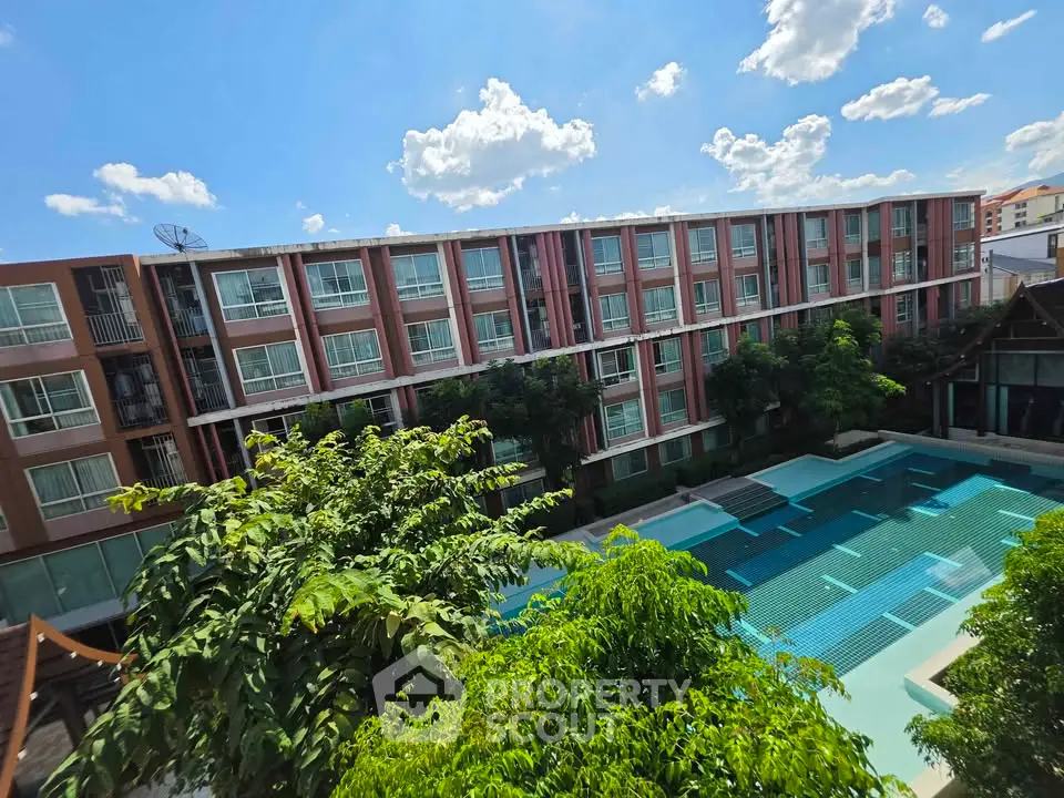 Modern apartment complex with large swimming pool and lush greenery under a clear blue sky.
