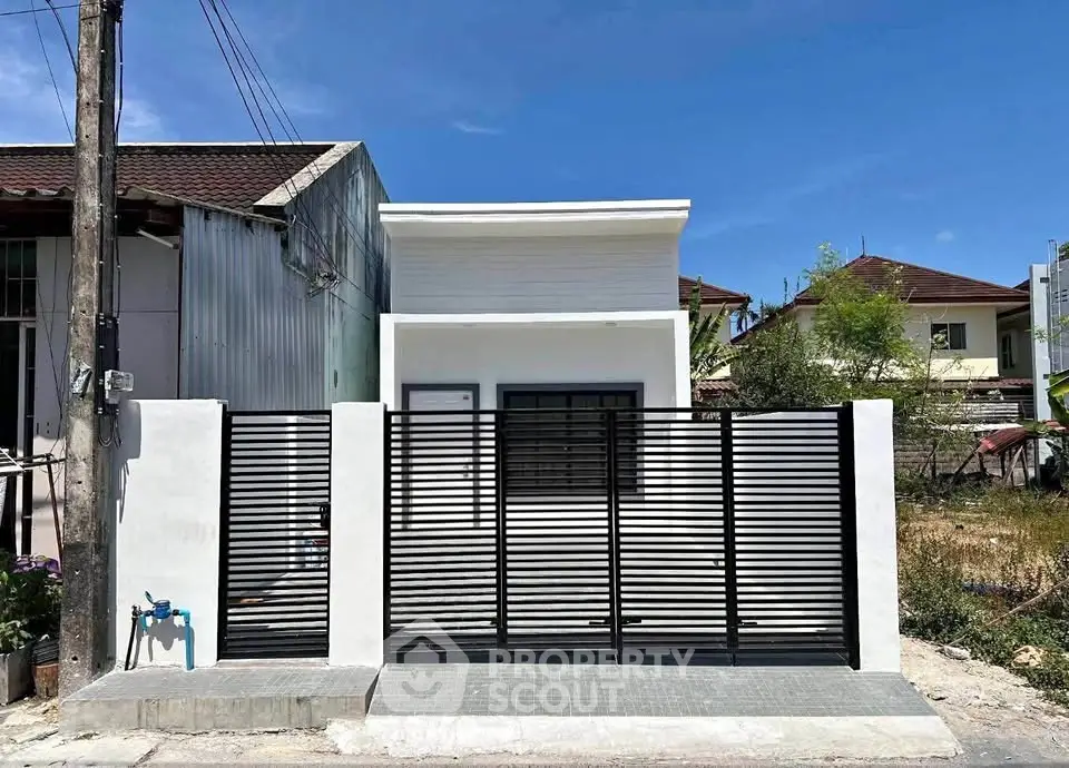 Modern minimalist house exterior with sleek black fence and white facade under clear blue sky.