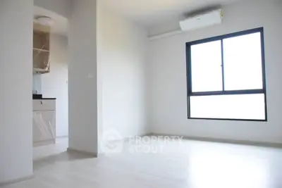 Bright minimalist apartment interior with large window and partial kitchen view.