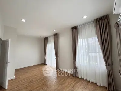 Spacious empty room with wooden flooring and large windows with curtains, perfect for customization.