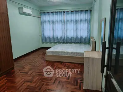 Spacious bedroom with wooden flooring and large window for natural light.