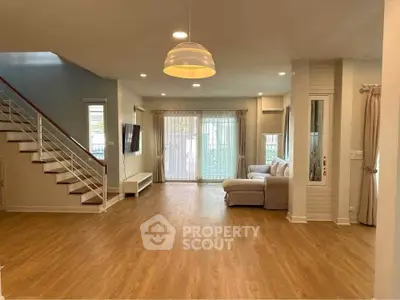 Spacious living room with wooden flooring and modern staircase in a bright, open-plan home.