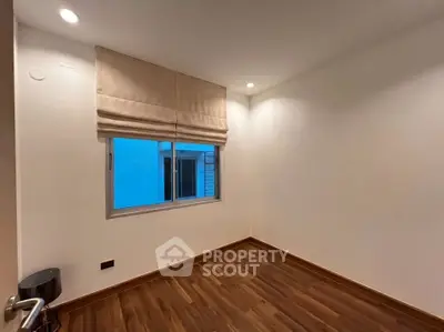 Spacious empty room with wooden flooring and window, ideal for customization.