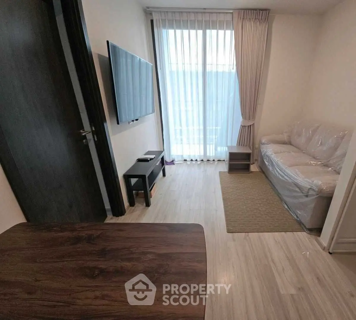 Cozy living room with natural light, modern TV setup, and elegant curtains.