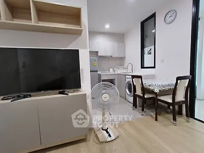 Modern living area with TV, fan, and compact kitchen in open layout apartment.