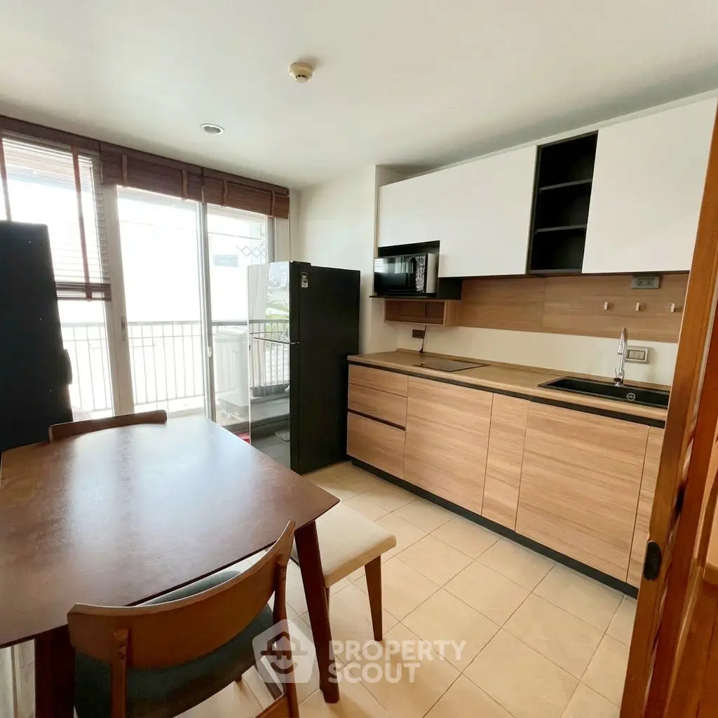 Modern kitchen with wooden cabinets and dining area, featuring a balcony view.