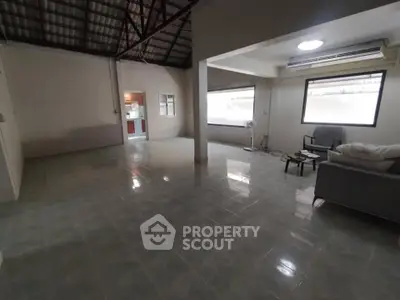 Spacious open-plan living room with tiled flooring and large windows, featuring modern furniture and air conditioning.