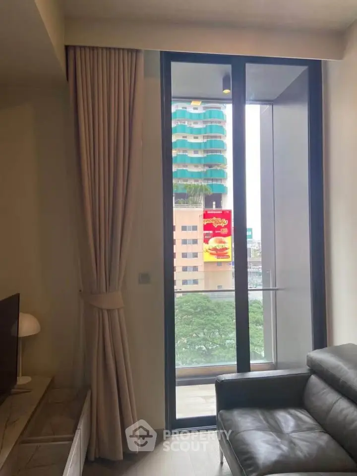 Modern living room with large window and city view, featuring elegant curtains and leather sofa.