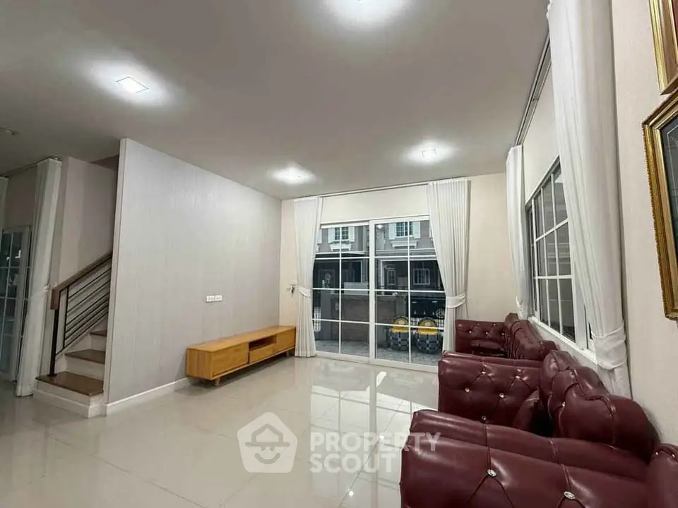 Spacious living room with elegant red leather sofas and large windows offering natural light.