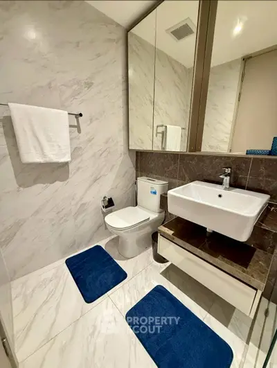 Modern bathroom with sleek design, featuring a white sink, toilet, and marble walls for a luxurious feel.