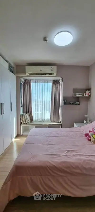 Cozy bedroom with large window and pink bedding, featuring ample storage and natural light.