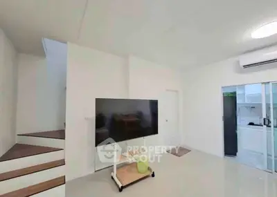 Modern living room with sleek TV setup and minimalist design, featuring a staircase and air conditioning.