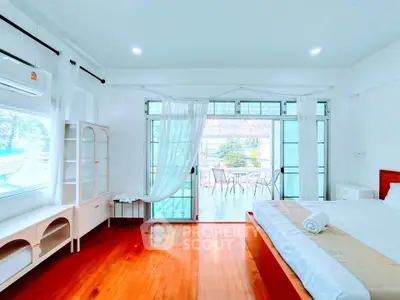 Spacious bedroom with large windows and balcony access, featuring elegant wooden flooring and modern decor.