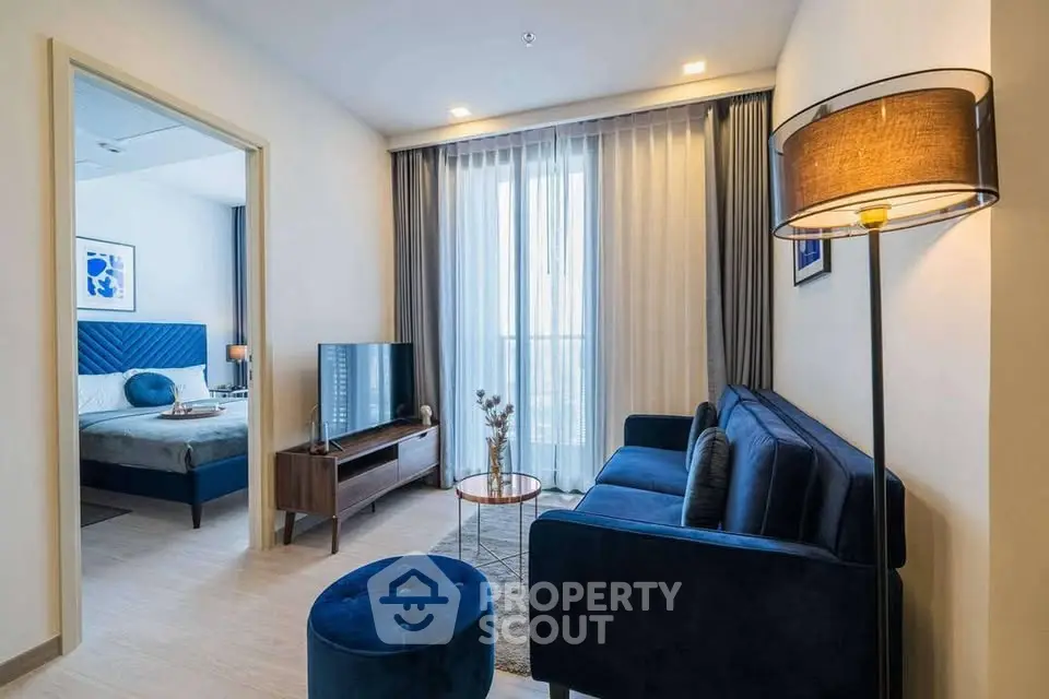 Modern living room with blue sofa and natural light, adjacent to a stylish bedroom.