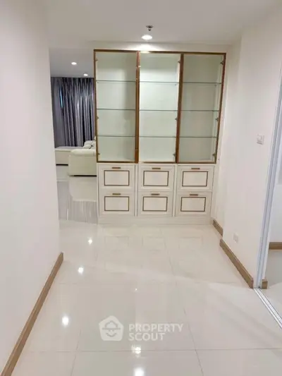 Spacious hallway leading to a modern living room with elegant glass cabinet and plush seating.