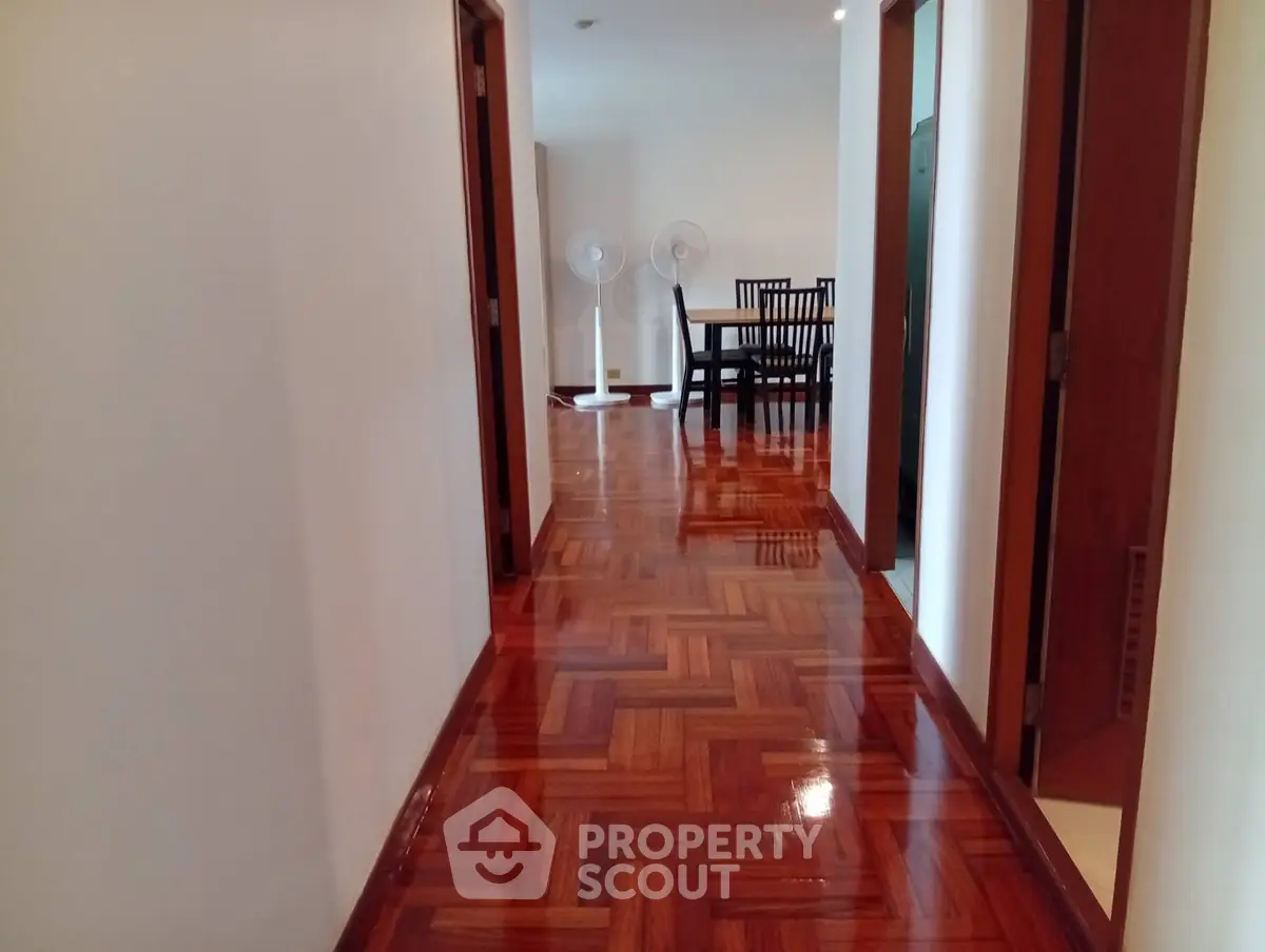 Spacious hallway with polished wooden floors leading to a dining area with elegant furniture.