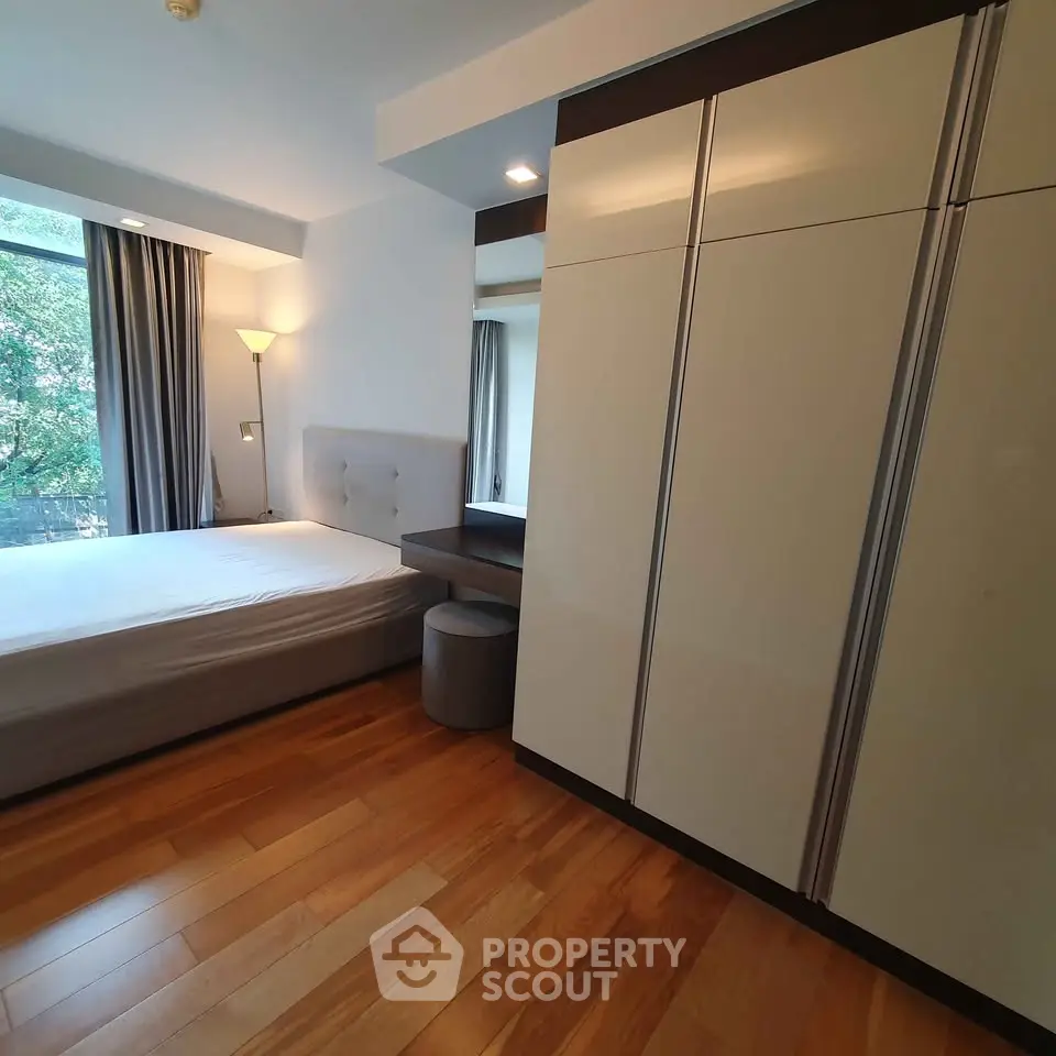 Modern bedroom with wooden flooring and large wardrobe, featuring natural light from window.