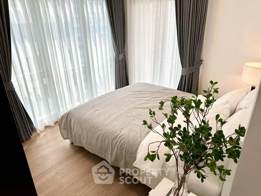 Cozy bedroom with large windows and elegant curtains, featuring a comfortable bed and stylish decor.