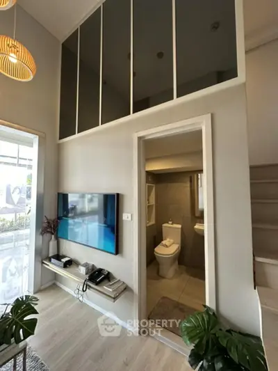 Modern living room with high ceiling and adjacent bathroom, featuring stylish decor and natural light.