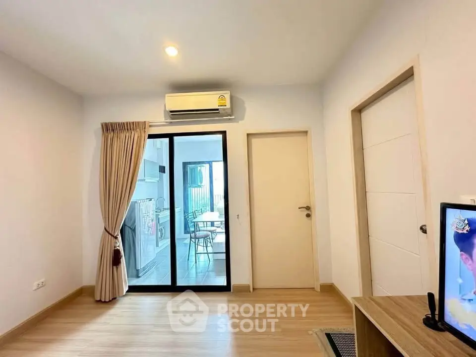 Modern living room with sliding glass doors leading to a bright dining area, featuring sleek wooden flooring and air conditioning.